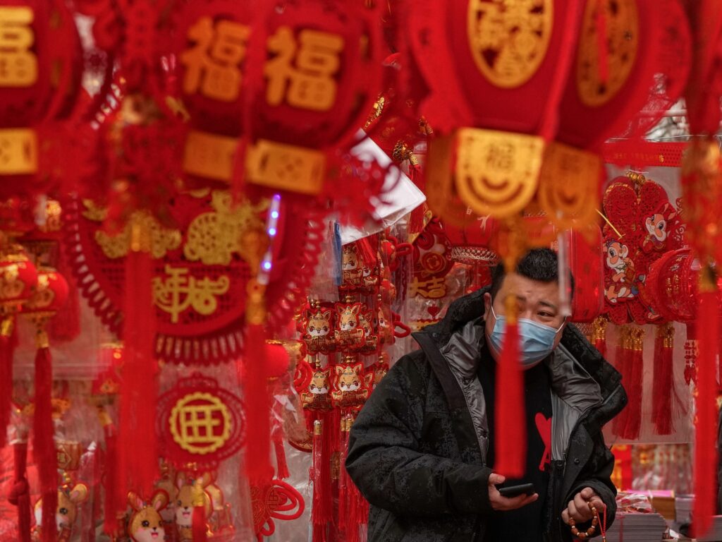 A man wearing a face mask shops for Chinese Lunar New Year decorations at a pavement store in Beijing, Saturday, Jan. 7, 2023. China has suspended or closed the social media accounts of more than 1,000 critics of the government's policies on the COVID-19 outbreak, as the country moves to further open up. (AP Photo/Andy Wong)