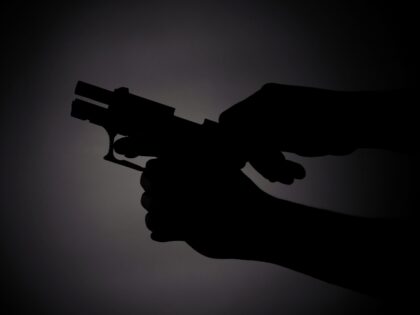 black silhouette of a male reloading a gun in the dark