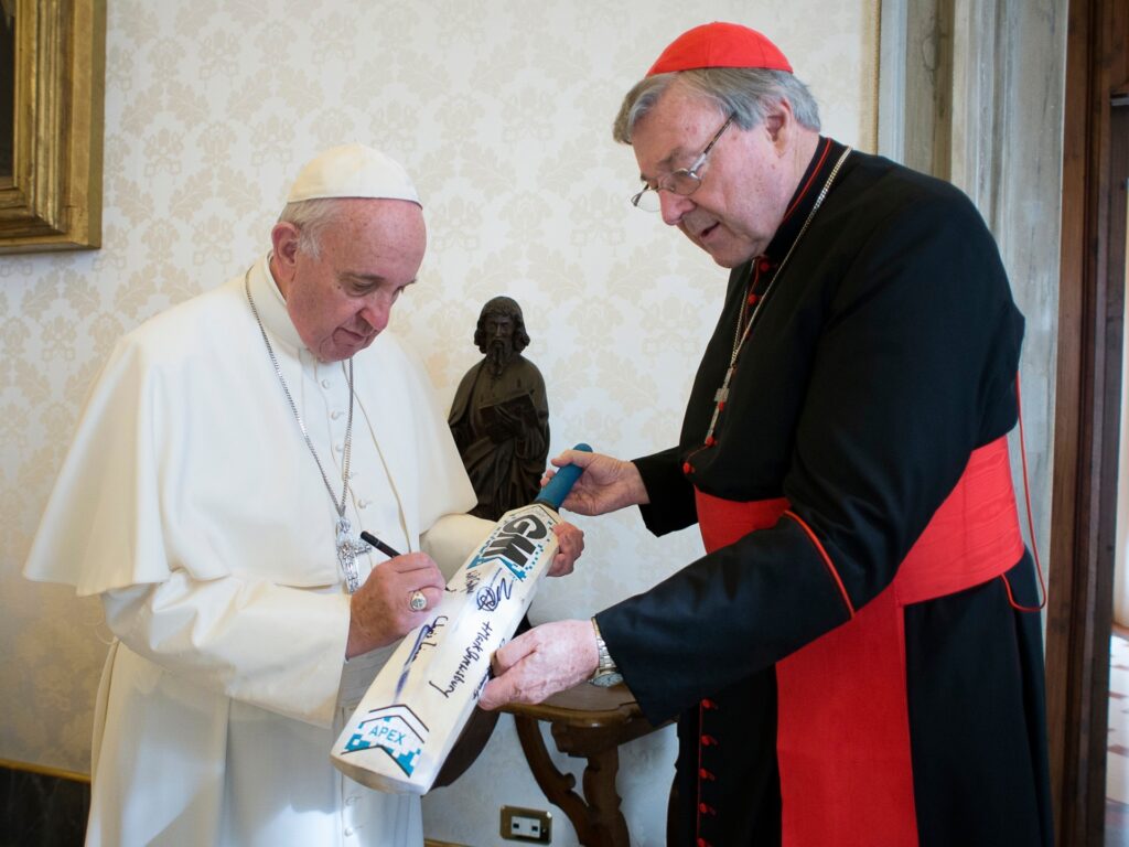 FILE -- In this photo taken October 29, 2015, Pope Francis signs a cricket bat he received from Cardinal George Pell, at the Vatican.  Cardinal George Pell, chief financial adviser to Pope Francis, has been charged in his native Australia with multiple counts of 