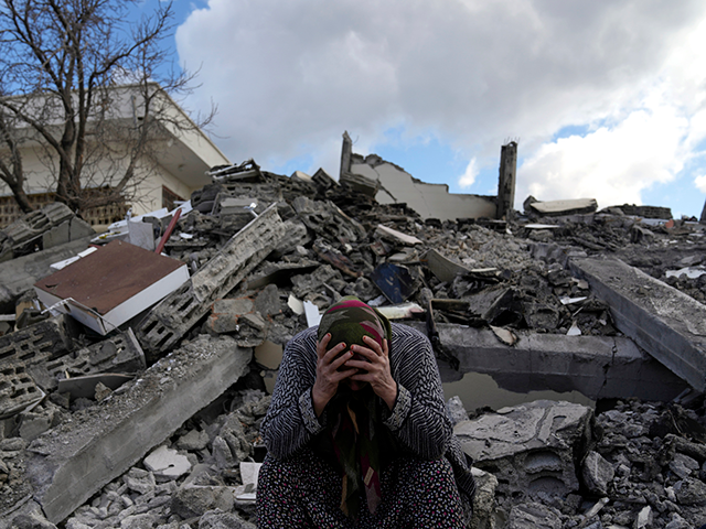A woman sits on the rubble as emergency rescue teams search for people under the remains o
