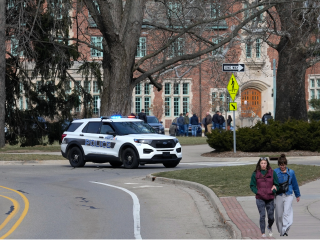 A police vehicle blocks a road as students walk on the Michigan State University campus in