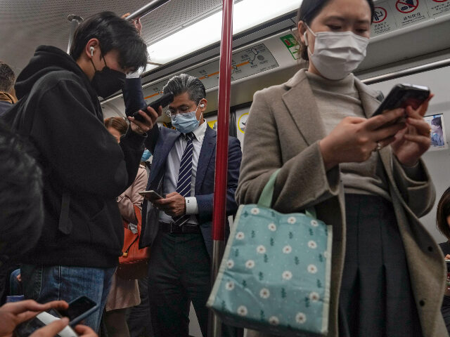 Commuters wearing face masks browse their smartphones as they ride on a subway train in Ho