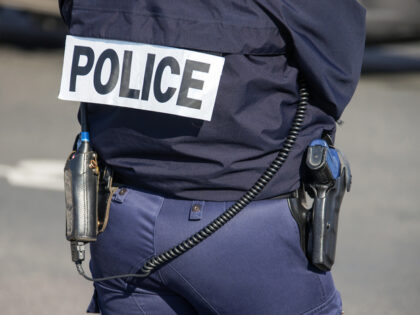 The back of the police officer with the inscription "POLICE" with a gun and a walkie-talkie. French policeman in outfit, view from the back on the street of Paris. France,