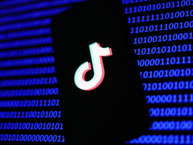 TikTok logo displayed on a phone screen and a binary code displayed on a screen are seen i