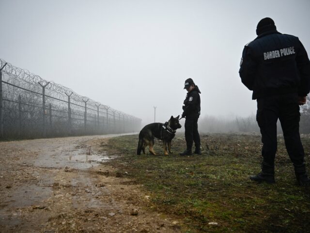 Bulgarian border police officers patrol with a dog in front of the border fence on the Bul