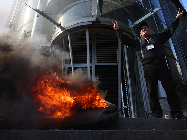 A Lebanese protester flashes the V-sign for victory and shouts slogans as others vandalise