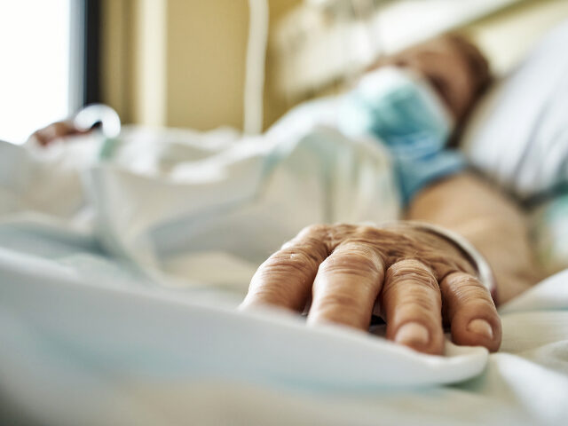 Senior woman wearing mask infected by coronavirus on hospital bed receiving medicine by drip. Close-up fingers of the senior patient ´s hand while she is sleeping. Horizontal photo