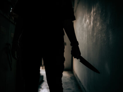 The shadow of a female murderer stood terrifyingly holding a knife and lit from behind.Sca