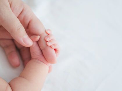 Mother uses her hand to hold her baby's tiny hand to make him feeling her love, warm and secure. Newborn.