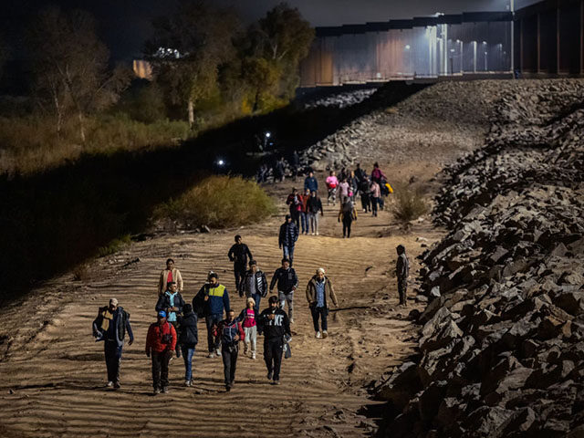 YUMA, ARIZONA - DECEMBER 30: Immigrants walk along the U.S.-Mexico border barrier on their