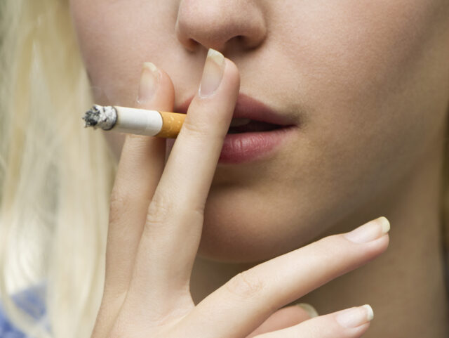 Young woman smoking cigarette, cropped