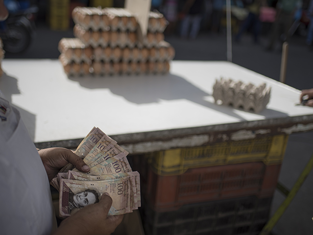 A worker counts 100-bolivar notes at an egg stand in Caracas, Venezuela, on Monday, Dec. 1
