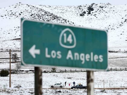 ACTON, CALIFORNIA - FEBRUARY 26: People walk in the snow near a freeway sign pointing to the city of Los Angeles on February 26, 2023 near Acton, California. A major storm, which carried a rare blizzard warning for parts of Southern California, delivered heavy snowfall to the mountains with some …