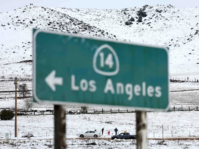 ACTON, CALIFORNIA - FEBRUARY 26: People walk in the snow near a freeway sign pointing to t