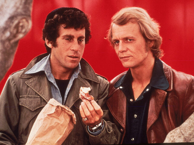 Actor Paul Michael Glaser (L) holds a donut, standing beside David Soul in a still from th