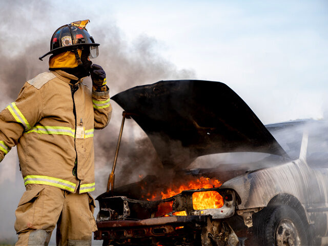 Firefighter standing in front of a burned car - stock photo