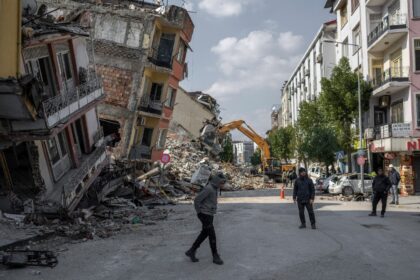 People walk next to damaged buildings in Antakya