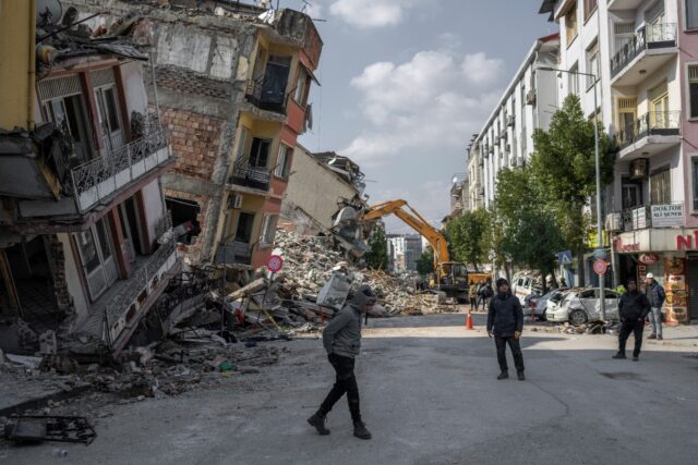 People walk next to damaged buildings in Antakya