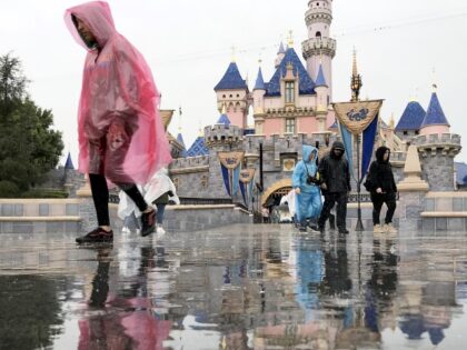 ANAHEIM, CA - MARCH 12: Disneyland guests walk past the Sleeping Beauty Castle while visiting Disneyland amid rain showers in Anaheim, Calif., on March 12, 2020. Disneyland will temporary close the Disneyland Resort in Anaheim in response to the expanding threat posed by the Coronavirus Pandemic. The closure takes effect …