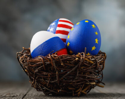 Three Easter eggs in a nest painted in colors of the flags of Russia, America and European Union on a wooden table, close-up