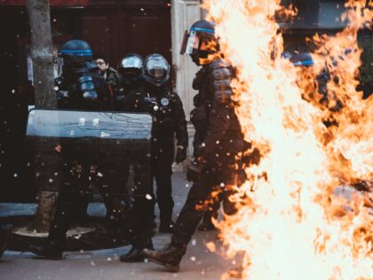 Riot police march behind a lit garbage can fire after clashes with thugs and black blocs a