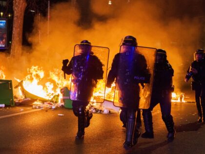 Riot police run past a fire lit by demonstrators on Boulevard Massena during a protest against pension reformat at Porte de Choisy in Paris, France, on Saturday, March 18, 2023. France will press ahead with an overhaul of its retirement system despite street protests and no-confidence votes planned for Monday, …