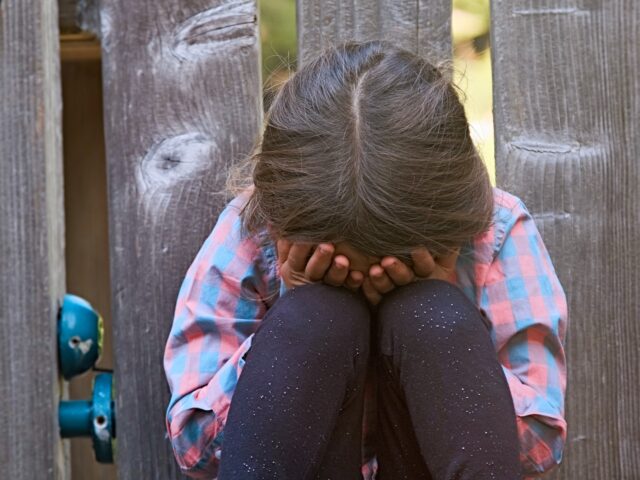 Crying child girl sitting on the floor covering her face - stock photo