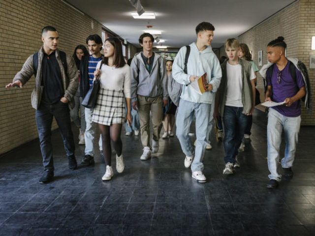 A group of high school students walking down the corridor together on their way to class.