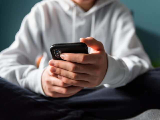 Close up of hands of teen boy in white sweater texting on phone.