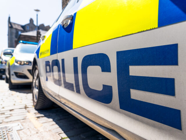 The word 'Police' below the fluorescent decals on a police car on a UK street, with other