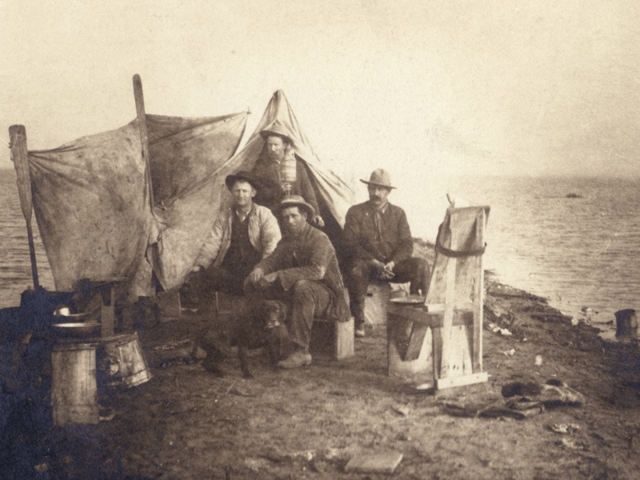 A group of unidentified men and a dog camping at the shores of Tulare Lake. This image is