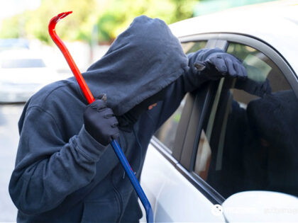 Thief in a balaclava stealing woman's bag from car - stock photo