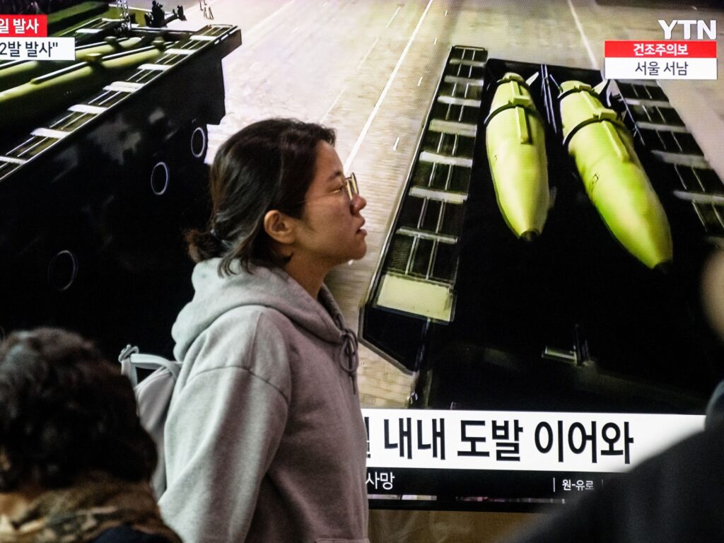 A woman walks past a television showing a news broadcast with file footage of missiles during a North Korean military parade, at a railway station in Seoul on March 27, 2023. - North Korea fired two short-range ballistic missiles on March 27, South Korea's military said, the latest in its flurry of weapons tests in recent weeks. (Photo by Anthony WALLACE / AFP) (Photo by ANTHONY WALLACE/AFP via Getty Images)