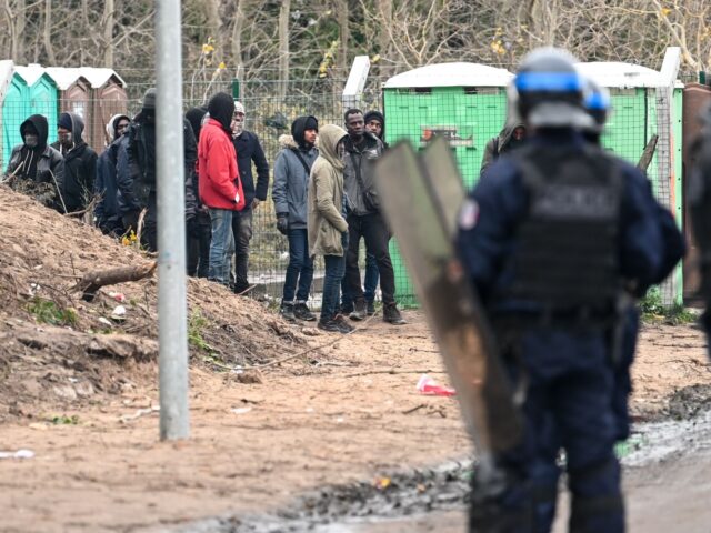 Police stand next to migrants at the makeshift camp in Calais, northern France, on Novembe