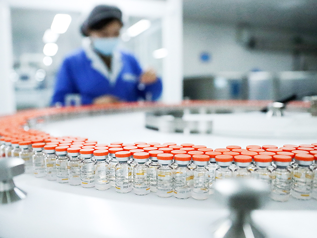 A staff member checks tags on vials of inactivated COVID-19 vaccine at a packing line of S