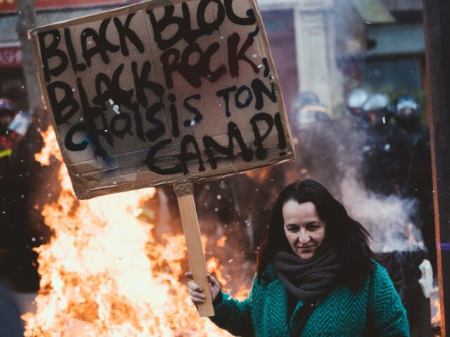A demonstrator holds a sign reading ''Black bloc, BlackRock, choose your side'' in front of a rubbish fire as tens of thousands of people take part in a new day of protest in Paris on 7 March 2023, the sixth since the social movement began. On the call of the …