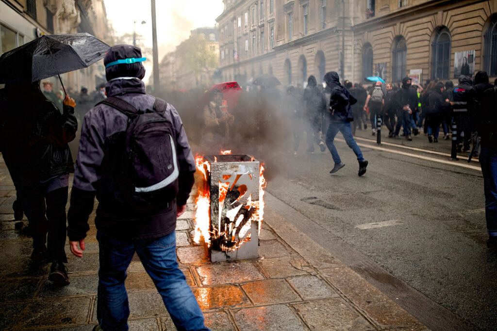 PARIS, FRANCE - 2023/04/13: A protester walks past one of the rubbish bins set on fire during the demonstration. Citizens took to the streets to protest against pension reform in Paris. (Photo by Marco Cordone/SOPA Images/LightRocket via Getty Images)