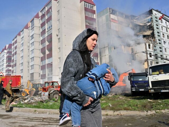 TOPSHOT - A woman walks past damaged residential buildings as she carries a child in Uman,