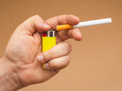 close up view of a man holds a cigarette, and a steel gas lighter.