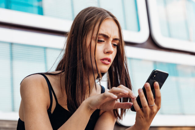 Reading Bad News on Mobile Phone. Young teenage woman checking her messages and social med