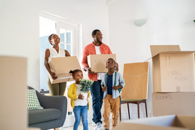 Beautiful african american family with two children carrying boxes in a new home. Cheerful