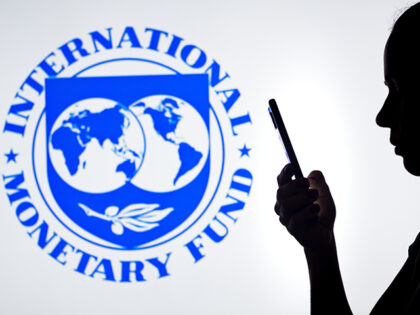 A woman's silhouette holds a smartphone with the International Monetary Fund (IMF) lo