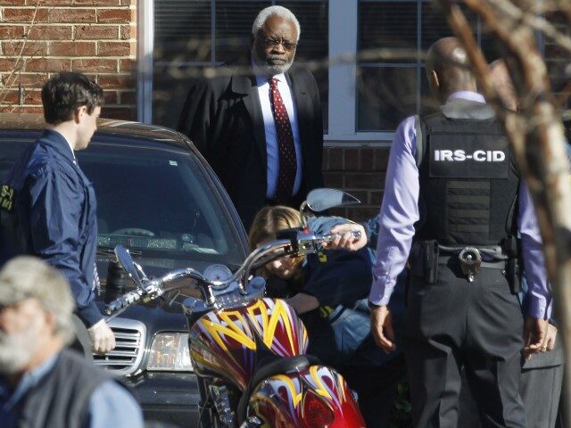 Attorney Fred Cooke, rear center, watches as agents seize a motorcycle outside the house o