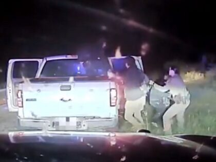 A female Texas DPS trooper grabs migrants by the arm to prevent them from fleeing into the