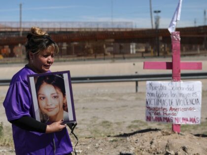 Susana Montes shows a photo of her daughter Maria Guadalupe Perez Montes, a victim of disappearance, trafficking, and femicide, next to a pink cross placed on the banks of the Rio Grande, in front of the United States border wall in Ciudad Juarez, State of Chihuahua, Mexico, on March 8, …