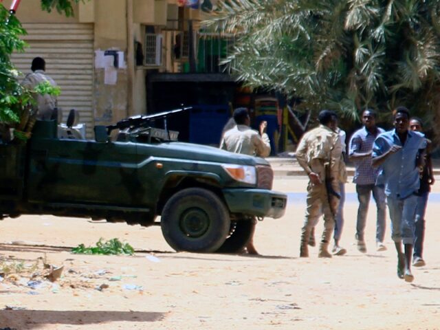 People run past a military vehicle in Khartoum on April 15, 2023, amid reported clashes in
