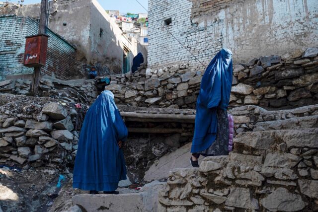 Burqa-clad Afghan women climb a stony path to their homes in the Shor Bazar area of the ca