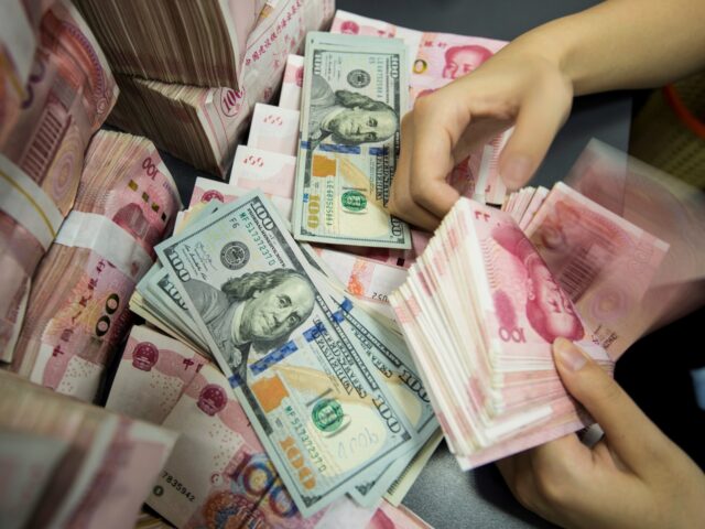 A Chinese bank employee counts 100-yuan notes and US dollar bills at a bank counter in Nan