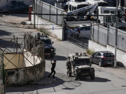 A Palestinian man throws stones at a convoy of Israeli military vehicles, during a raid in the West Bank city of Nablus, Thursday, May 4, 2023. The Israeli military says it has killed three Palestinians wanted for an attack last month on a car near a Jewish West Bank settlement …