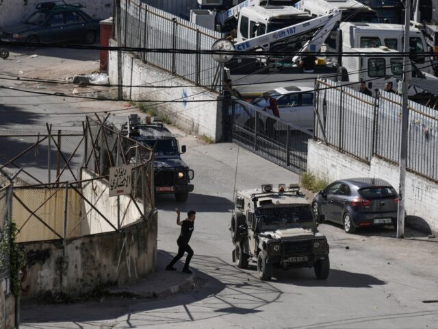 A Palestinian man throws stones at a convoy of Israeli military vehicles, during a raid in